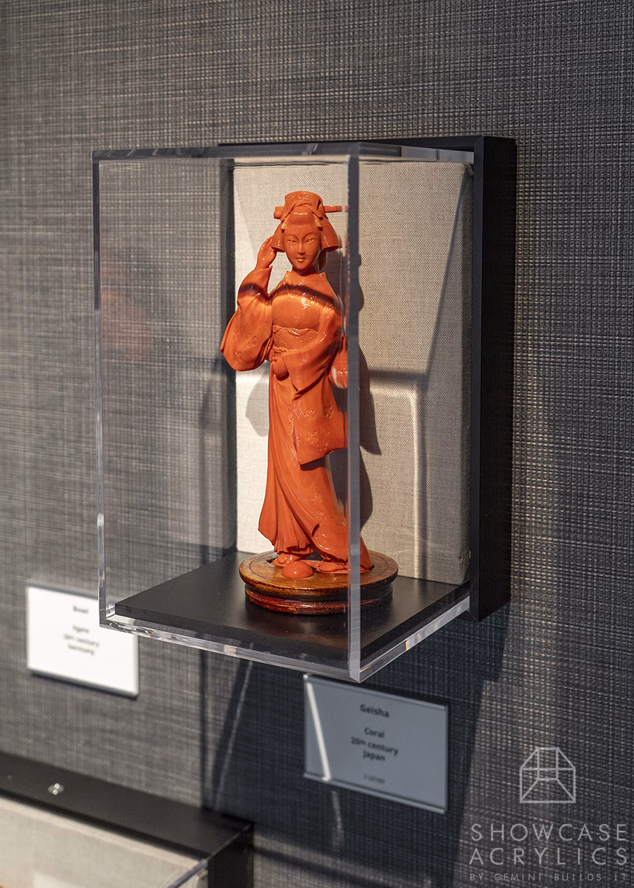 Terracotta Geisha statue in a glass display case mounted on a textured wall.
